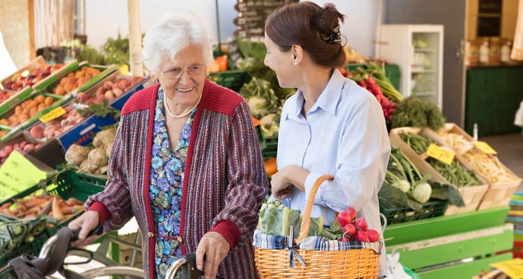 Two women shopping at an outdoor market with fresh produce