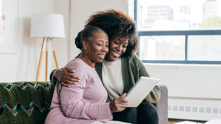 Two women smiling and looking at a tablet in a cozy living room