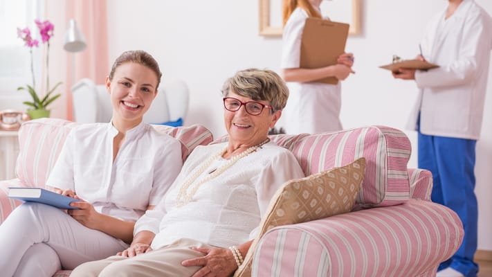 Caregiver and resident smiling in a comfortable living room.