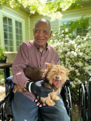 A resident smiling and holding a dog in a garden
