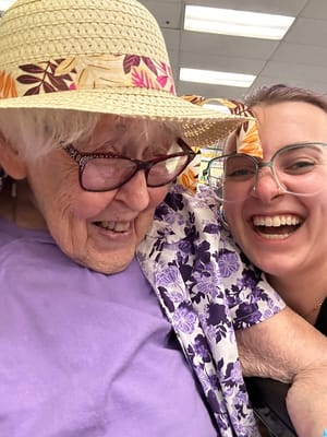 A woman smiling with a senior resident in a colorful hat