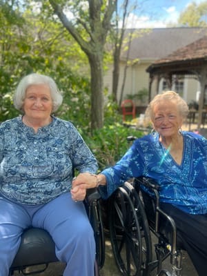 Two elderly residents holding hands in a garden area