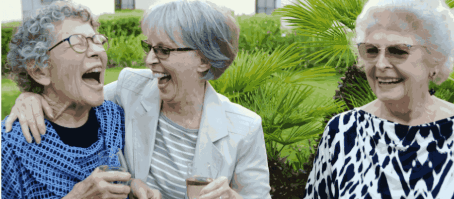Three elderly women laughing together outdoors