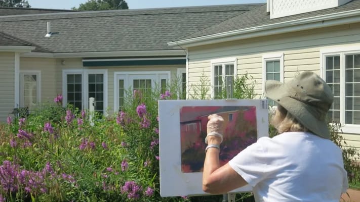 A resident painting outside surrounded by flowers