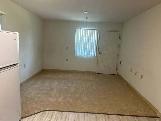 Empty living area with a window, door, and refrigerator