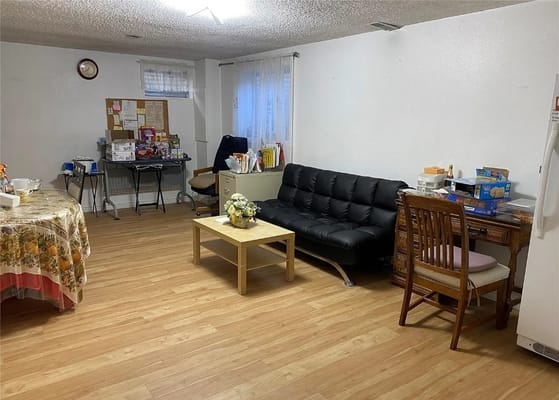 Cozy living room with a black couch, wooden chairs, and a table.