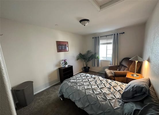A cozy bedroom with a bed, armchair, and window.