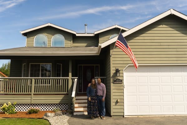 A couple standing in front of a residential building with an American flag