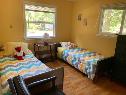 A cozy bedroom with two beds, a lamp, and a teddy bear.