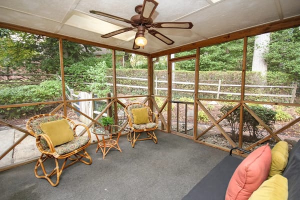 A cozy sunroom featuring patterned chairs and a glass table with a plant.