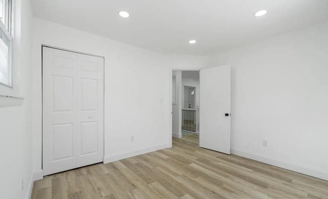 A bright bedroom with wooden flooring and white walls.