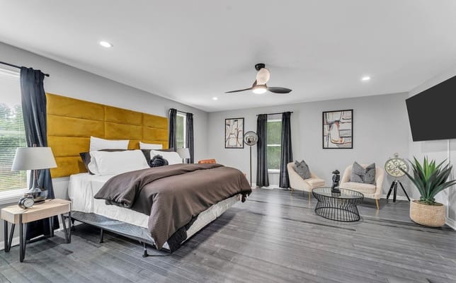 A stylish bedroom with a yellow headboard, modern decor, and large windows.