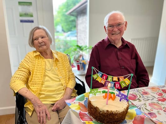 Elderly couple celebrating a birthday with cake and decorations.
