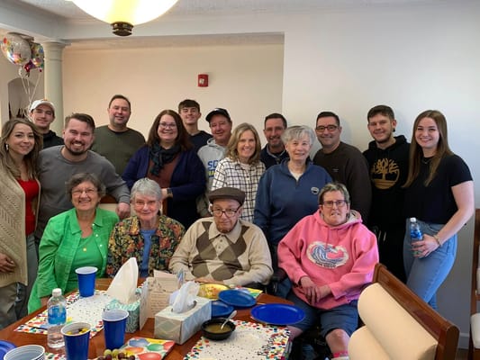 A group of residents and family members smiling together in a communal room.