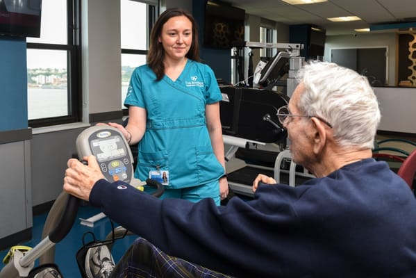 A staff member assisting an elderly man with a fitness machine