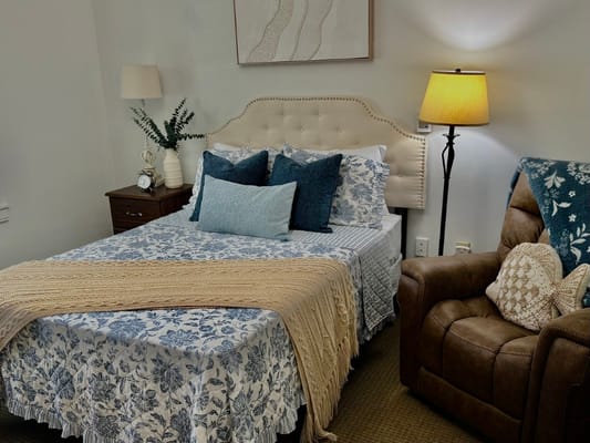 A cozy, well-decorated resident room with a bed and armchair