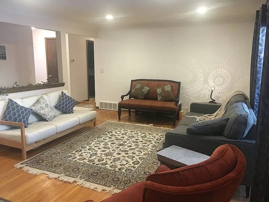 A cozy living room with various seating options and a decorative rug.