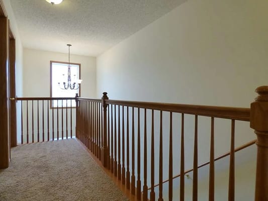 Well-lit hallway with wooden railing and chandelier