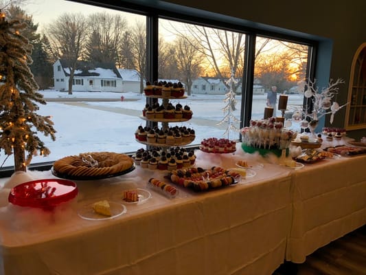 A beautifully arranged dessert table with various sweets in front of large windows at sunset.
