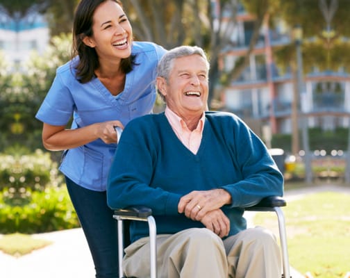 A caregiver and resident enjoying time outdoors in a wheelchair