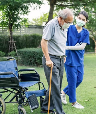Senior resident assisted by staff in a garden area