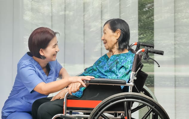 A caregiver interacts warmly with a resident in a wheelchair