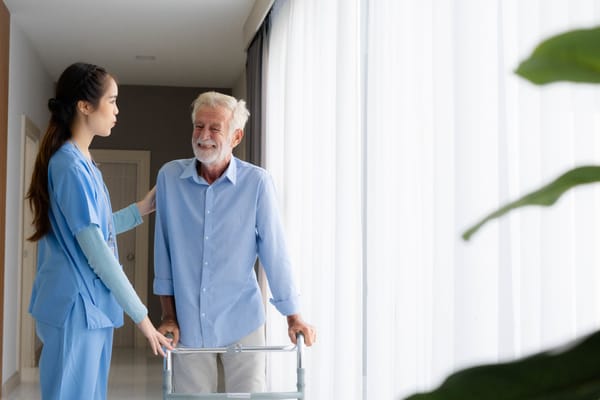 A caregiver assisting a senior resident in a bright hallway