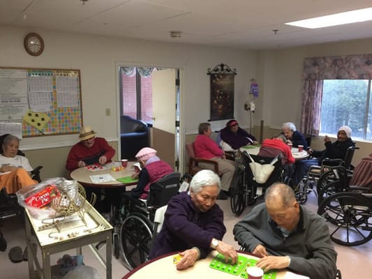 Seniors playing bingo in a common room at a healthcare facility.