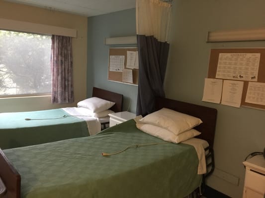 Two twin beds in a shared room with green blankets and a window.