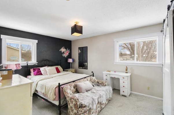 A cozy bedroom featuring a bed, sitting area, and natural light.