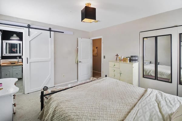 A well-decorated bedroom with a bed, dresser, and sliding door to a bathroom.