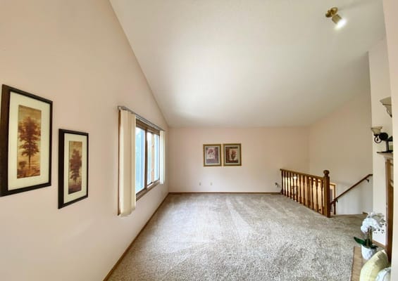 A spacious living room with carpeted flooring and framed artwork on the walls.