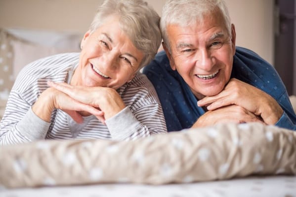 Two smiling seniors posing together on a bed