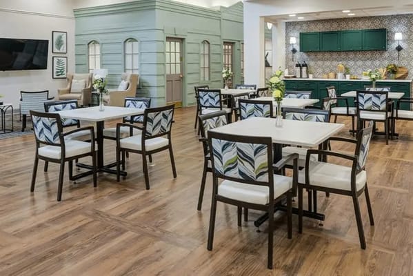 Dining space with tables, chairs, and a green kitchen in the background