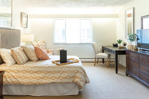 A comfortable bedroom with a bed, chair, desk, and television