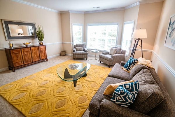A comfortable living room featuring a glass coffee table, gray sofa, and armchairs with decorative pillows.