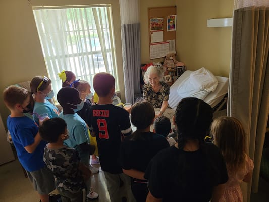 A senior woman interacts with a group of children in a care facility room