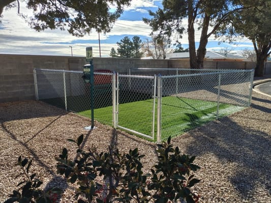 A fenced dog park with artificial grass and a waste station at Kingdom of the Sun Retirement Center.