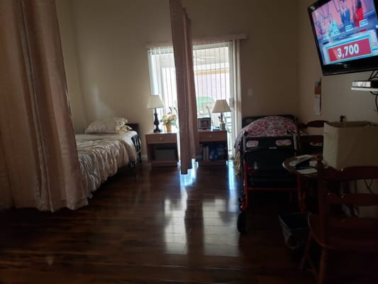 Interior view of a private room with a bed, wheelchair, and furnishings.