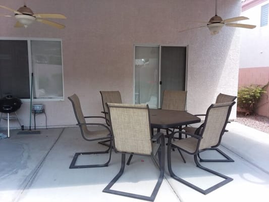 Metal patio table surrounded by six chairs in a shaded area.