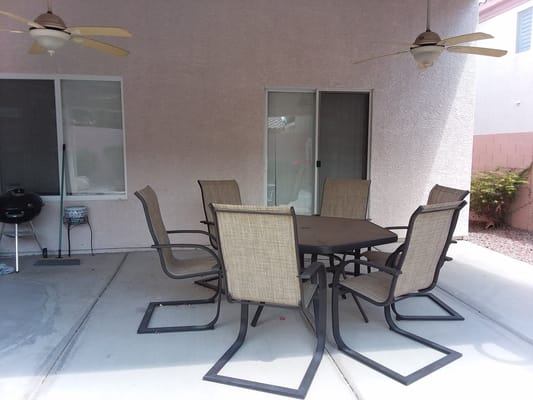 Metal patio table surrounded by six chairs in a shaded area.