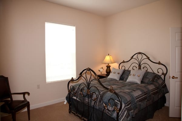 A well-furnished bedroom with a bed, lamp, and chair.
