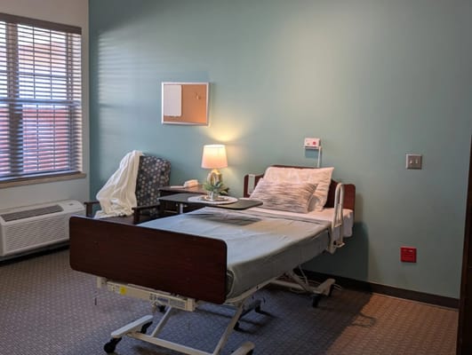 Bedroom with hospital bed, chair, and lamp.