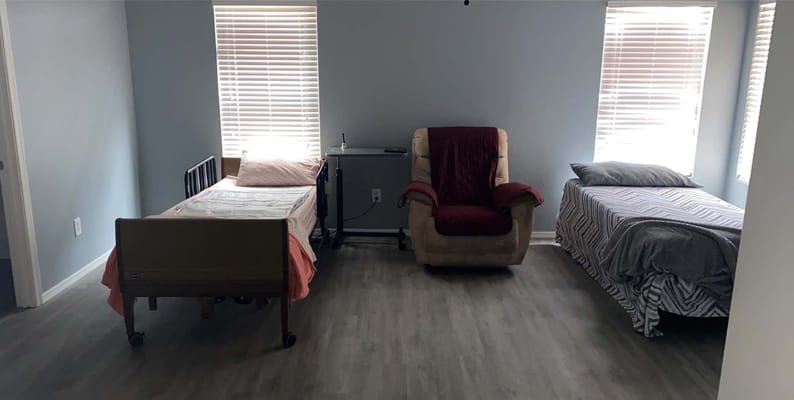 A shared resident room with two beds and a recliner
