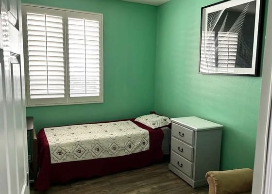 Private bedroom with green walls and a bed covered in a quilt.