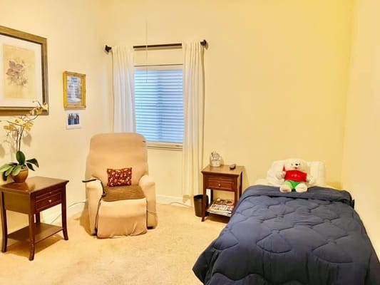 A well-lit bedroom featuring a bed, chair, and decorative items.