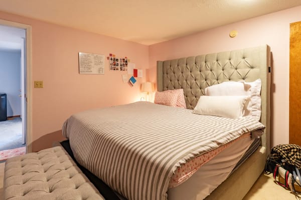 A cozy bedroom with a tufted gray bed and pink walls.