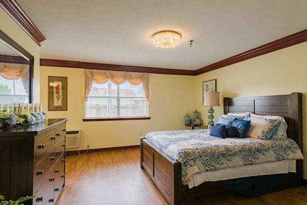 A well-furnished private resident room with a bed and dresser