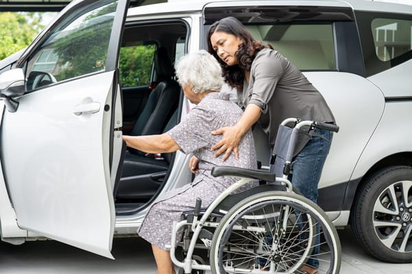 Caregiver assisting elderly woman in wheelchair into a vehicle
