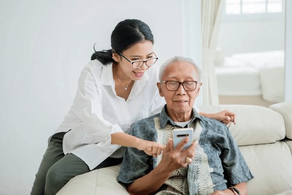 A caregiver assisting a senior resident on a smartphone in a living area